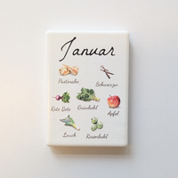 Saisonkalender Kühlschrankmagneten aus Keramik. Jeder Magnet repräsentiert einen Monat von Januar bis Dezember mit deutscher Beschriftung in geschwungener Schrift. Auf der cremefarbenen Oberfläche sind detailreiche, farbige Illustrationen von saisonalem Obst und Gemüse mit den jeweiligen Namen abgebildet.