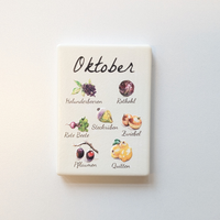 Saisonkalender Kühlschrankmagneten aus Keramik. Jeder Magnet repräsentiert einen Monat von Januar bis Dezember mit deutscher Beschriftung in geschwungener Schrift. Auf der cremefarbenen Oberfläche sind detailreiche, farbige Illustrationen von saisonalem Obst und Gemüse mit den jeweiligen Namen abgebildet.