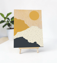 Abstrakte Illustration einer Berglandschaft mit gelber Sonne in Blau- und Gelbtönen, gedruckt auf einer natürlichen 9mm Birkensperrholzplatte im Format 30x40 cm.