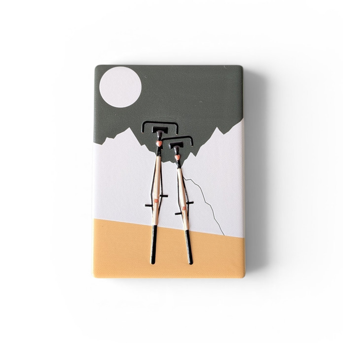 Rechteckiger Keramik-Kühlschrankmagnet (7x5 cm) mit zwei schwarzen Fahrrädern im Vordergrund vor weißen Bergen, einem graugrünen Himmel mit weißem Vollmond und einem ockergelben Boden mit spürbarem 3D-Relief.