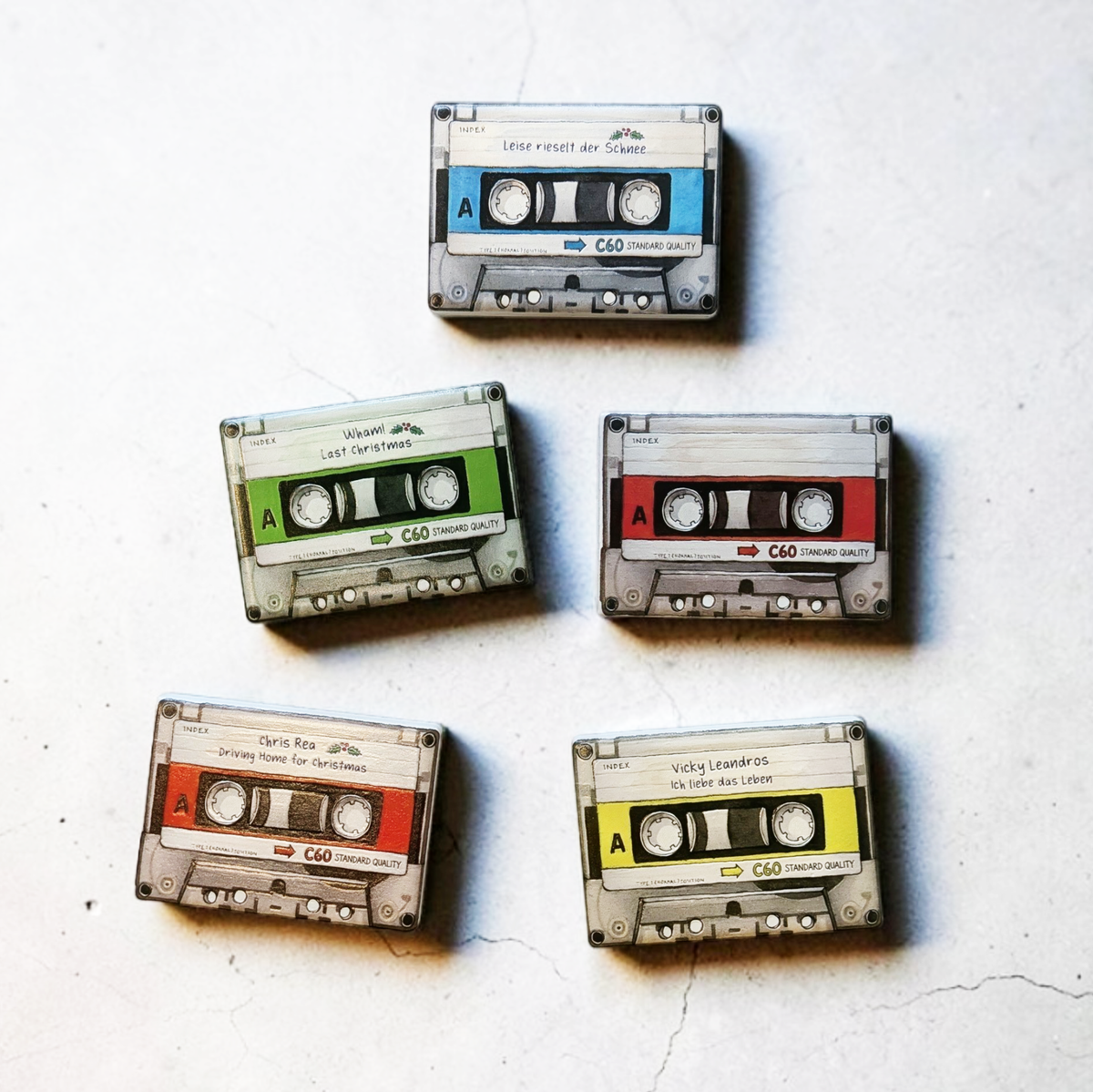 Rechteckiger Keramik-Kühlschrankmagnet (7x5 cm) im Retro-Musikkassetten-Design mit seidenmatter Glasur. Die Kassette verfügt über ein personalisierbares Beschriftungsfeld für Wunschtexte (wahlweise mit kleinem Mistelzweig) sowie spürbar erhabene Bandspulen und Kanten im 0,9 mm tiefen 3D-Relief.