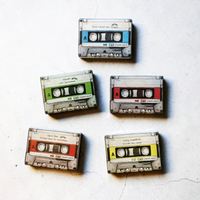 Rechteckiger Keramik-Kühlschrankmagnet (7x5 cm) im Retro-Musikkassetten-Design mit seidenmatter Glasur. Die Kassette verfügt über ein personalisierbares Beschriftungsfeld für Wunschtexte (wahlweise mit kleinem Mistelzweig) sowie spürbar erhabene Bandspulen und Kanten im 0,9 mm tiefen 3D-Relief.