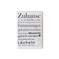 Rechteckiger Keramik-Kühlschrankmagnet (7x5 cm) mit seidenmatter Glasur. Auf hellem Grund steht der schwarze Spruch 'Zuhause ist wo die Liebe wohnt...' neben einer kleinen Haus-Illustration mit Herz im spürbaren 3D-Relief.