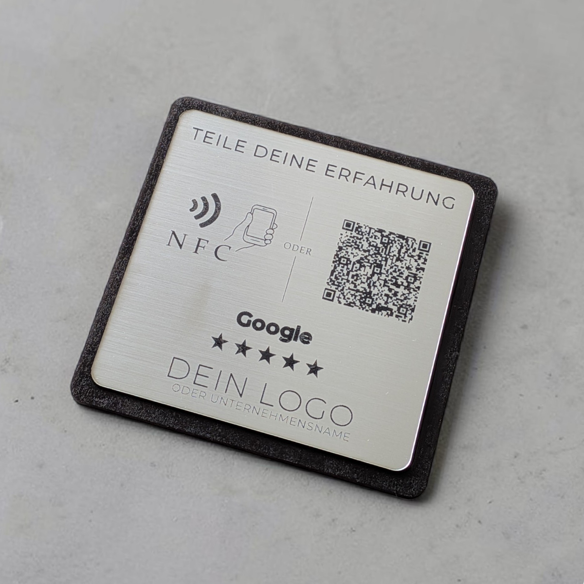 Ein quadratischer oder rechteckiger Tischaufsteller zur Kundenbewertung. Auf der Vorderseite befindet sich oben das farbige Google-Logo, gefolgt von der Aufforderung 'Bewerte uns auf Google'. Im Zentrum ist ein scannbarer QR-Code abgebildet. Unten rechts signalisiert ein Wellen-Symbol die integrierte NFC-Funktion zum kontaktlosen Scannen mit dem Smartphone.