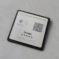 Ein quadratischer oder rechteckiger Tischaufsteller zur Kundenbewertung. Auf der Vorderseite befindet sich oben das farbige Google-Logo, gefolgt von der Aufforderung 'Bewerte uns auf Google'. Im Zentrum ist ein scannbarer QR-Code abgebildet. Unten rechts signalisiert ein Wellen-Symbol die integrierte NFC-Funktion zum kontaktlosen Scannen mit dem Smartphone.