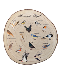 Eine runde Holzscheibe aus hellem Paulownia-Holz mit echter Baumrinde. Auf der Oberfläche sind im Kreis 14 verschiedene heimische Vogelarten wie Blaumeise, Rotkehlchen und Specht mit ihren Namen farbig aufgedruckt. Oben steht der geschwungene Schriftzug "Heimische Vögel". Der Druck hat ein fühlbares 0,3 mm Relief.