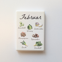 Saisonkalender Kühlschrankmagneten aus Keramik. Jeder Magnet repräsentiert einen Monat von Januar bis Dezember mit deutscher Beschriftung in geschwungener Schrift. Auf der cremefarbenen Oberfläche sind detailreiche, farbige Illustrationen von saisonalem Obst und Gemüse mit den jeweiligen Namen abgebildet.