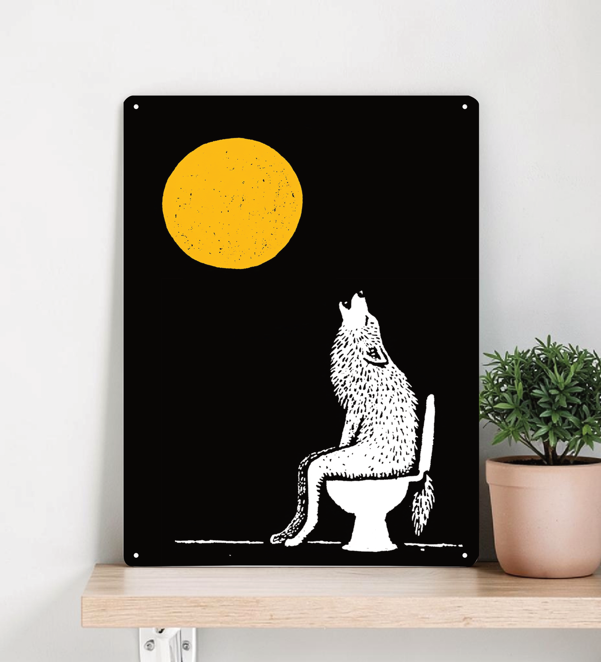 Ein hochformatiges, schwarzes Metallschild steht dekorativ auf einem hellen Holzregal vor einer beigen Wand. Das Motiv zeigt einen großen, strukturierten gelben Vollmond und die weiße Silhouette eines Wolfs, der auf einer Toilette sitzt und nach oben heult. 