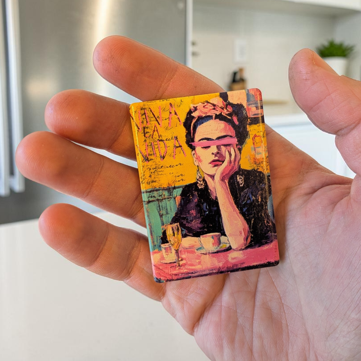 Künstlerisches Porträt einer Frau mit Blumen im Haar und einem pinkfarbenen Pinselstrich über den Augen. Im Hintergrund steht der Schriftzug „VIVA LA VIDA“ auf gelbem, strukturiertem Grund.