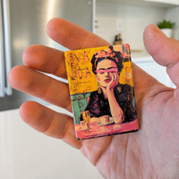 Künstlerisches Porträt einer Frau mit Blumen im Haar und einem pinkfarbenen Pinselstrich über den Augen. Im Hintergrund steht der Schriftzug „VIVA LA VIDA“ auf gelbem, strukturiertem Grund.
