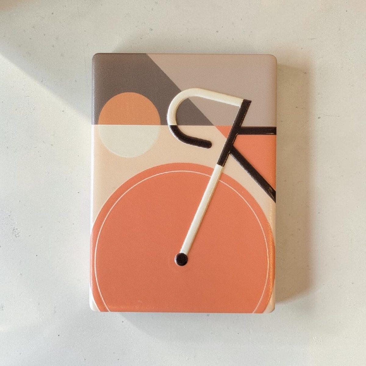 Rechteckiger Keramik-Kühlschrankmagnet im Bauhaus-Stil mit einem abstrahierten Fahrrad-Motiv. Die geometrischen Formen und Linien sind als fühlbares 0,9 mm Hochrelief ausgearbeitet, kombiniert mit Vintage-Farben und minimalistischer Typografie auf 7x5 cm.