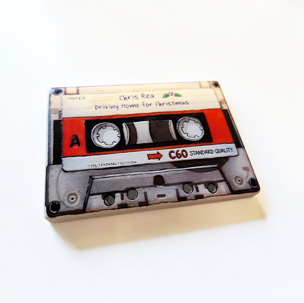 Rechteckiger Keramik-Kühlschrankmagnet (7x5 cm) im Retro-Musikkassetten-Design mit seidenmatter Glasur. Die Kassette verfügt über ein personalisierbares Beschriftungsfeld für Wunschtexte (wahlweise mit kleinem Mistelzweig) sowie spürbar erhabene Bandspulen und Kanten im 0,9 mm tiefen 3D-Relief.