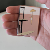 "Rechteckiger Keramik-Kühlschrankmagnet (7x5 cm) im Vintage-Stil. Abgebildet ist eine Frau im weißen Badeanzug, die mit einem gelben Schirm von einem dunklen Sprungturm springt. Der Hintergrund ist zweigeteilt in Altrosa und Cremeweiß mit spürbarem 3D-Relief."