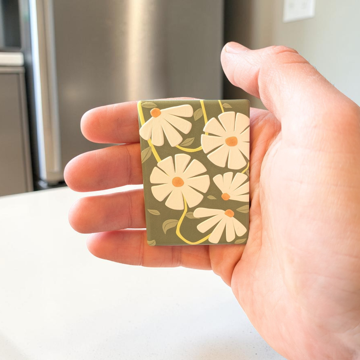 Rechteckiger Keramik-Kühlschrankmagnet (7x5 cm) in Salbeigrün mit einem spürbaren 3D-Relief aus weißen Gänseblümchen, gelben Blütenmitten und grünen Blattranken.