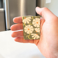Rechteckiger Keramik-Kühlschrankmagnet (7x5 cm) in Salbeigrün mit einem spürbaren 3D-Relief aus weißen Gänseblümchen, gelben Blütenmitten und grünen Blattranken.