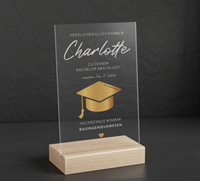 Transparenter Acrylglas-Aufsteller mit Holzsockel, personalisiert als Geschenk zum Abschluss. Zeigt goldene Doktorhut-Grafik, Namen, Studiengang und Hochschule in elegantem Design.