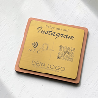 Quadratische, personalisierte Instagram-Follower-Platte aus graviertem Kunststoff in gebürsteter Gold-Optik auf Holzträger. Graviert mit 'Folge uns auf Instagram', NFC-Symbol, QR-Code und Logo.