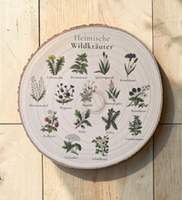 Kreisrunde, rustikale Holzscheibe mit natürlicher Rinde, auf die 16 detailreiche, farbige Vintage-Illustrationen heimischer Wildkräuter und Bäume mit ihren Namen im Kreis angeordnet gedruckt sind. In der Mitte steht der Titel „Heimische Wildkräuter“ in eleganter Schrift.