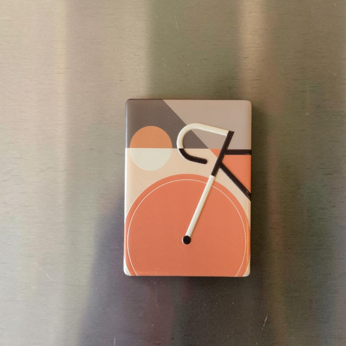 Rechteckiger Keramik-Kühlschrankmagnet im Bauhaus-Stil mit einem abstrahierten Fahrrad-Motiv. Die geometrischen Formen und Linien sind als fühlbares 0,9 mm Hochrelief ausgearbeitet, kombiniert mit Vintage-Farben und minimalistischer Typografie auf 7x5 cm.