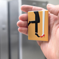 "Rechteckiger Keramik-Kühlschrankmagnet (7x5 cm) mit einem 3D-Relief. Zu sehen sind die Beine eines Paares: eine Person in roten High Heels und Herzchensocken, die andere in rot-weiß gestreiften Socken, auf hellem Hintergrund."