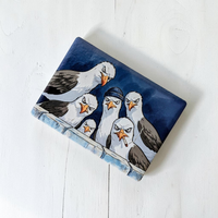 Rechteckiger Keramik-Kühlschrankmagnet (7x5 cm) im Querformat mit seidenmatter Glasur. Fünf grimmig dreinschauende Möwen, eine mit blauer Mütze und eine mit Zigarette, blicken über eine Mauer im spürbaren 3D-Relief.
