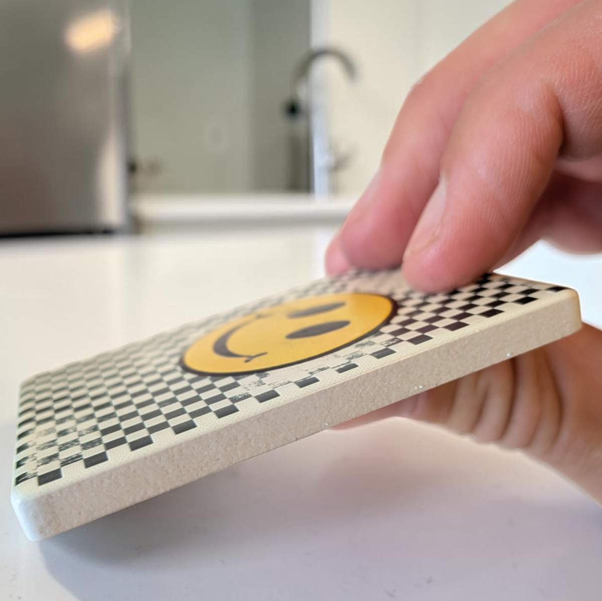 Rechteckiger weißer Keramikmagnet mit einem abstrahierten, gelben Smiley-Gesicht aus Quadraten. Die Oberfläche zeigt eine haptische Relief-Struktur und ein elegantes, seidenmattes Finish.