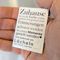 Rechteckiger Keramik-Kühlschrankmagnet (7x5 cm) mit seidenmatter Glasur. Auf hellem Grund steht der schwarze Spruch 'Zuhause ist wo die Liebe wohnt...' neben einer kleinen Haus-Illustration mit Herz im spürbaren 3D-Relief.