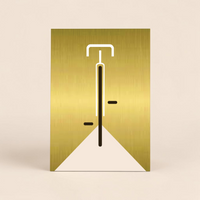 Minimalistische Bauhaus-Illustration eines Fahrrads in der Vorderansicht auf einer gebürsteten, gold-glänzenden Aluminiumplatte (Alu-Dibond). Das Design zeigt klare weiße und schwarze Linien vor einem edlen Metallhintergrund. Das Bild lehnt modern an einer weißen Wand zwischen zwei Zimmerpflanzen.