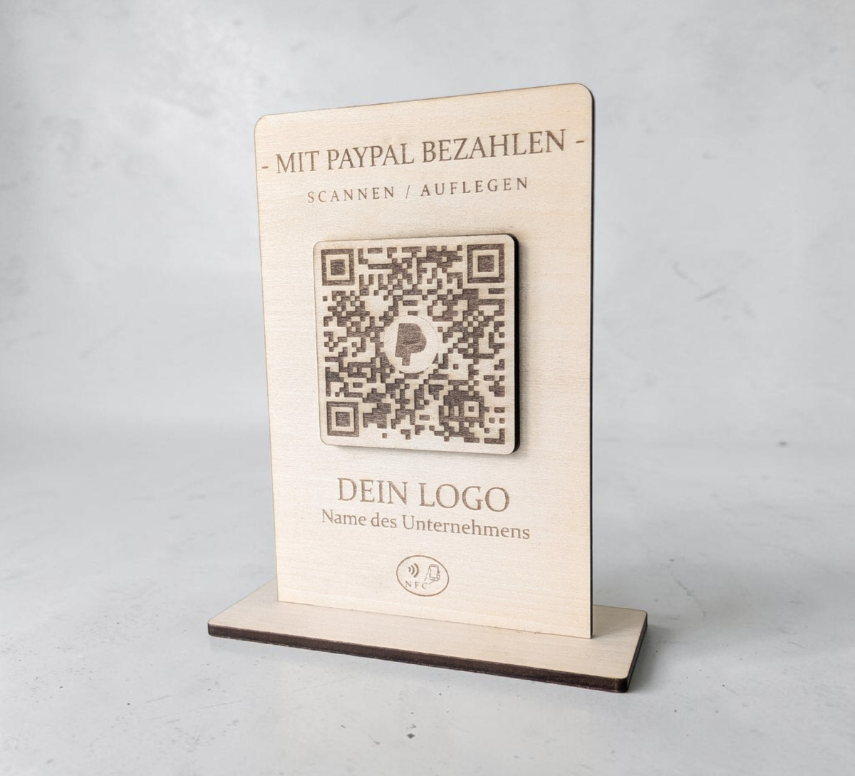 Rustikaler PayPal-Zahlungsaufsteller aus Holz mit graviertem QR-Code und NFC-Logo, der von einer Hand mit einem Smartphone berührt wird.