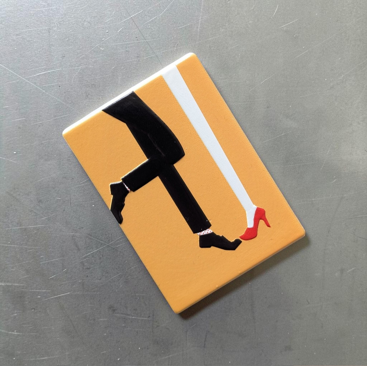 "Rechteckiger Keramik-Kühlschrankmagnet (7x5 cm) mit einem 3D-Relief. Zu sehen sind die Beine eines Paares: eine Person in roten High Heels und Herzchensocken, die andere in rot-weiß gestreiften Socken, auf hellem Hintergrund."