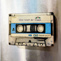 Rechteckiger Keramik-Kühlschrankmagnet (7x5 cm) im Retro-Musikkassetten-Design mit seidenmatter Glasur. Die Kassette verfügt über ein personalisierbares Beschriftungsfeld für Wunschtexte (wahlweise mit kleinem Mistelzweig) sowie spürbar erhabene Bandspulen und Kanten im 0,9 mm tiefen 3D-Relief.