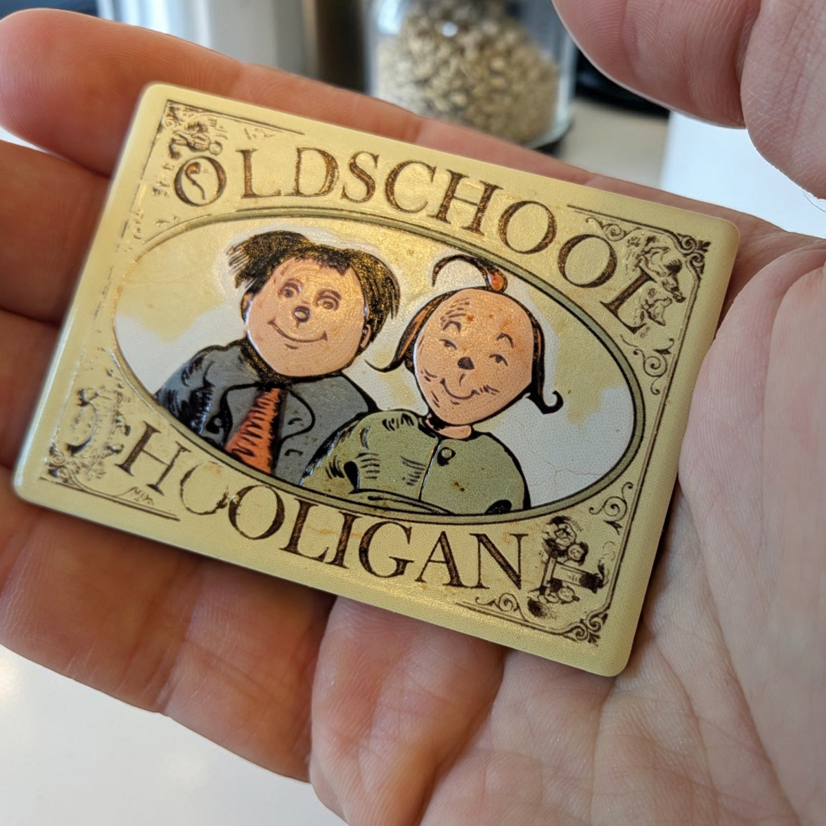 Rechteckiger Keramik-Kühlschrankmagnet (7x5 cm) im Vintage-Stil. Zu sehen ist ein ovales Medaillon mit den gezeichneten Gesichtern von Max und Moritz sowie dem Schriftzug 'OLDSCHOOL HOOLIGAN' im fühlbaren 3D-Relief.