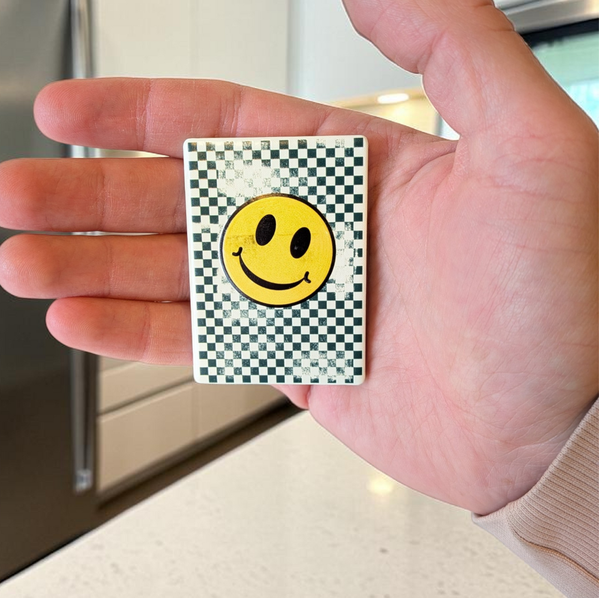 Rechteckiger weißer Keramikmagnet mit einem abstrahierten, gelben Smiley-Gesicht aus Quadraten. Die Oberfläche zeigt eine haptische Relief-Struktur und ein elegantes, seidenmattes Finish.
