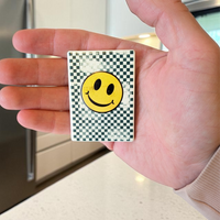 Rechteckiger weißer Keramikmagnet mit einem abstrahierten, gelben Smiley-Gesicht aus Quadraten. Die Oberfläche zeigt eine haptische Relief-Struktur und ein elegantes, seidenmattes Finish.
