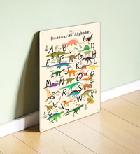 Farbenfrohes Dinosaurier ABC Poster für Kinder, dargestellt einmal als gerahmtes Papier-Poster und einmal als stabiles Metall-Blechschild mit abgerundeten Ecken und vier Bohrungen.