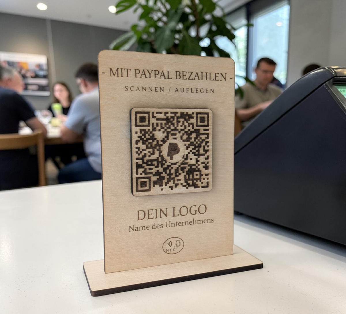 Rustikaler PayPal-Zahlungsaufsteller aus Holz mit graviertem QR-Code und NFC-Logo, der von einer Hand mit einem Smartphone berührt wird.