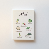 Saisonkalender Kühlschrankmagneten aus Keramik. Jeder Magnet repräsentiert einen Monat von Januar bis Dezember mit deutscher Beschriftung in geschwungener Schrift. Auf der cremefarbenen Oberfläche sind detailreiche, farbige Illustrationen von saisonalem Obst und Gemüse mit den jeweiligen Namen abgebildet.