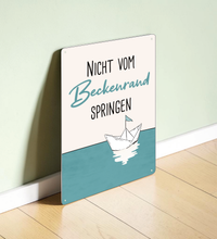 Rechteckiges Retro-Blechschild aus Metall mit dem Spruch „Nicht vom Beckenrand springen“, hochwertige Haptik, vier Eckbohrungen, vor weißem Hintergrund im Badezimmer-Stil.