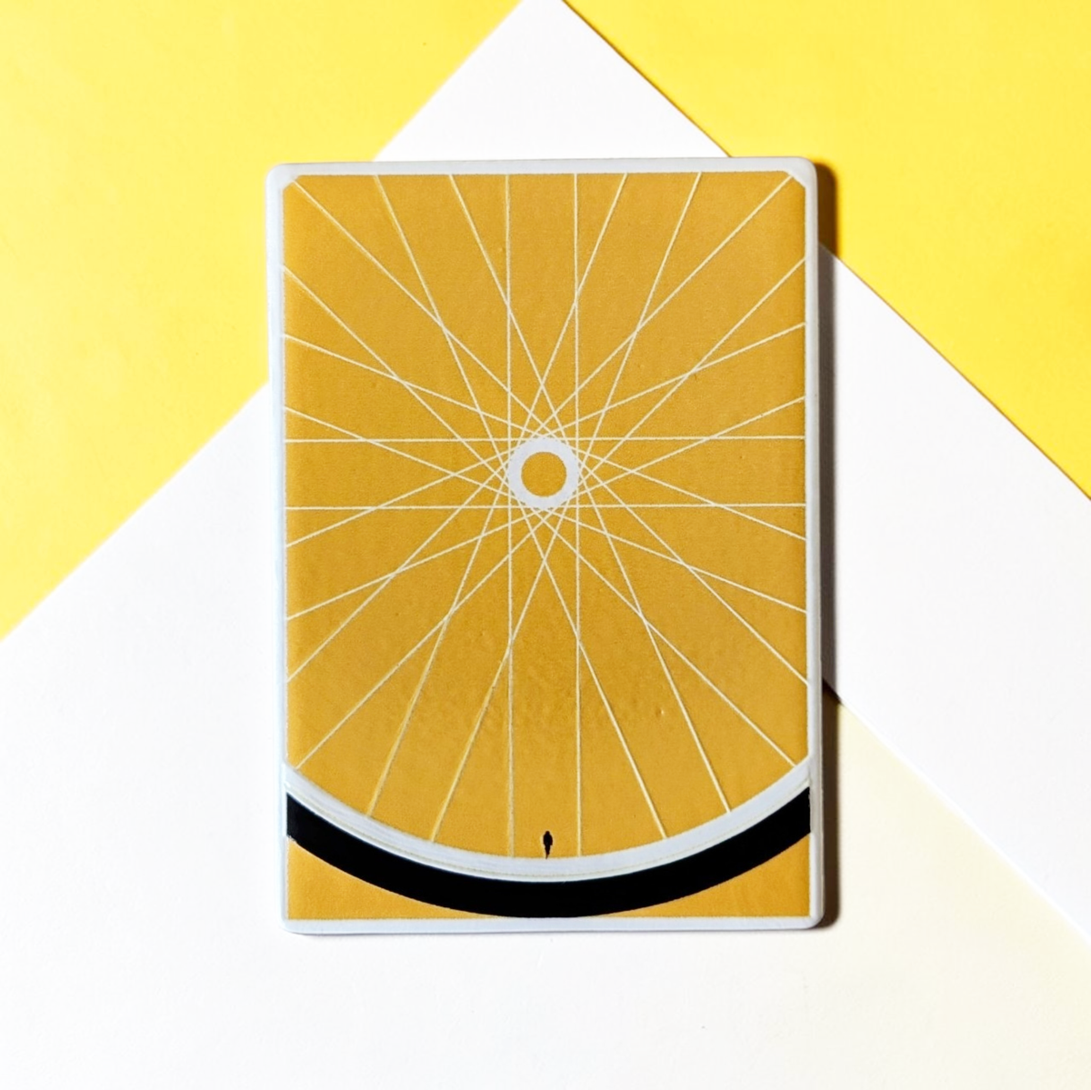 Rechteckiger Keramik-Kühlschrankmagnet (7x5 cm) in warmem Gelb. Gezeigt wird ein minimalistisches Fahrradrad mit feinen weißen Speichen, einem schwarzen Reifen am unteren Rand und einer winzigen menschlichen Silhouette im spürbaren 3D-Relief.