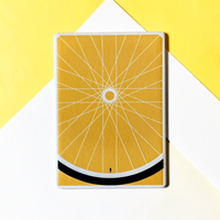 Rechteckiger Keramik-Kühlschrankmagnet (7x5 cm) in warmem Gelb. Gezeigt wird ein minimalistisches Fahrradrad mit feinen weißen Speichen, einem schwarzen Reifen am unteren Rand und einer winzigen menschlichen Silhouette im spürbaren 3D-Relief.