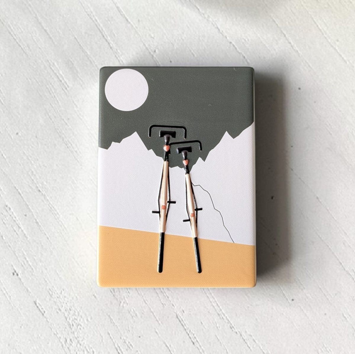 Rechteckiger Keramik-Kühlschrankmagnet (7x5 cm) mit zwei schwarzen Fahrrädern im Vordergrund vor weißen Bergen, einem graugrünen Himmel mit weißem Vollmond und einem ockergelben Boden mit spürbarem 3D-Relief.
