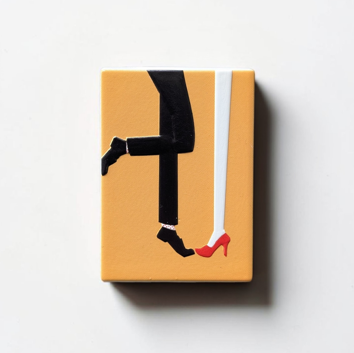 "Rechteckiger Keramik-Kühlschrankmagnet (7x5 cm) mit einem 3D-Relief. Zu sehen sind die Beine eines Paares: eine Person in roten High Heels und Herzchensocken, die andere in rot-weiß gestreiften Socken, auf hellem Hintergrund."
