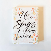Rechteckiger Keramik-Kühlschrankmagnet (7x5 cm) mit seidenmatter Glasur. Auf hellem Grund mit zarten orange-gelben Aquarell-Blumen steht der schwarze Handlettering-Schriftzug 'Who sings prays twice' im spürbaren 3D-Relief