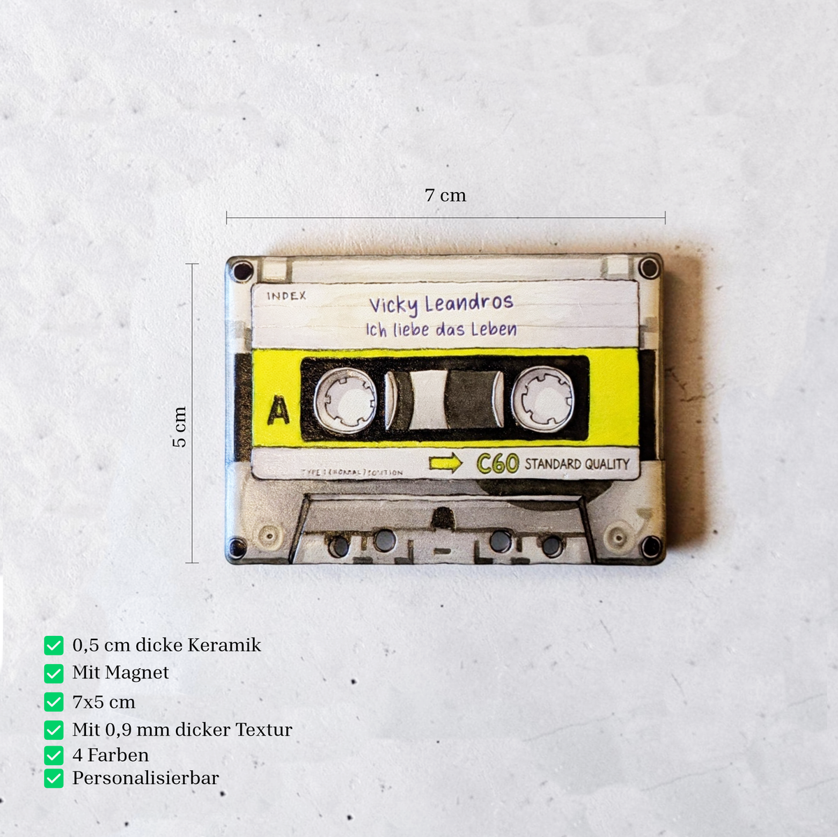 Rechteckiger Keramik-Kühlschrankmagnet (7x5 cm) im Retro-Musikkassetten-Design mit seidenmatter Glasur. Die Kassette verfügt über ein personalisierbares Beschriftungsfeld für Wunschtexte (wahlweise mit kleinem Mistelzweig) sowie spürbar erhabene Bandspulen und Kanten im 0,9 mm tiefen 3D-Relief.