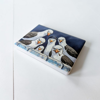 Rechteckiger Keramik-Kühlschrankmagnet (7x5 cm) im Querformat mit seidenmatter Glasur. Fünf grimmig dreinschauende Möwen, eine mit blauer Mütze und eine mit Zigarette, blicken über eine Mauer im spürbaren 3D-Relief.