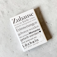 Rechteckiger Keramik-Kühlschrankmagnet (7x5 cm) mit seidenmatter Glasur. Auf hellem Grund steht der schwarze Spruch 'Zuhause ist wo die Liebe wohnt...' neben einer kleinen Haus-Illustration mit Herz im spürbaren 3D-Relief.
