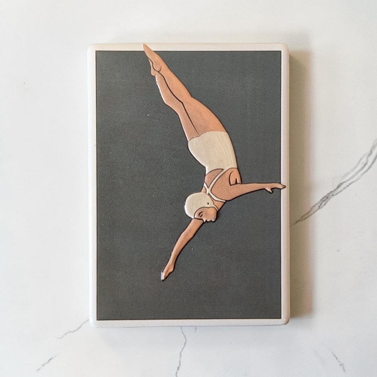 Rechteckiger weißer Keramikmagnet mit einer minimalistischen Illustration einer Turmspringerin im Sprung. Das Motiv hat ein fühlbares Relief und eine edle, seidenmatte Oberfläche.