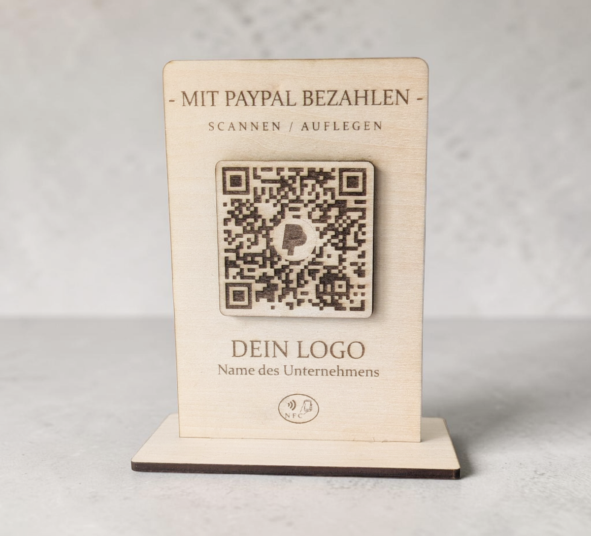 Rustikaler PayPal-Zahlungsaufsteller aus Holz mit graviertem QR-Code und NFC-Logo, der von einer Hand mit einem Smartphone berührt wird.
