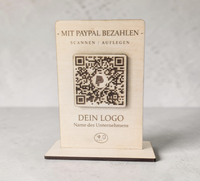 Rustikaler PayPal-Zahlungsaufsteller aus Holz mit graviertem QR-Code und NFC-Logo, der von einer Hand mit einem Smartphone berührt wird.
