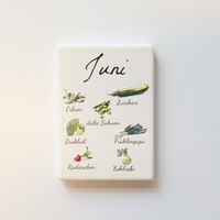 Saisonkalender Kühlschrankmagneten aus Keramik. Jeder Magnet repräsentiert einen Monat von Januar bis Dezember mit deutscher Beschriftung in geschwungener Schrift. Auf der cremefarbenen Oberfläche sind detailreiche, farbige Illustrationen von saisonalem Obst und Gemüse mit den jeweiligen Namen abgebildet.